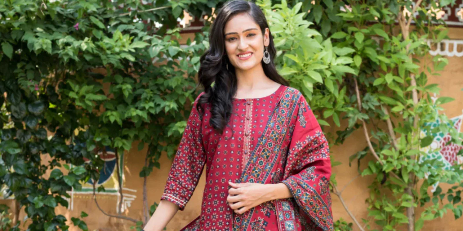 Smiling woman wearing a red printed kurti with matching dupatta in a garden setting