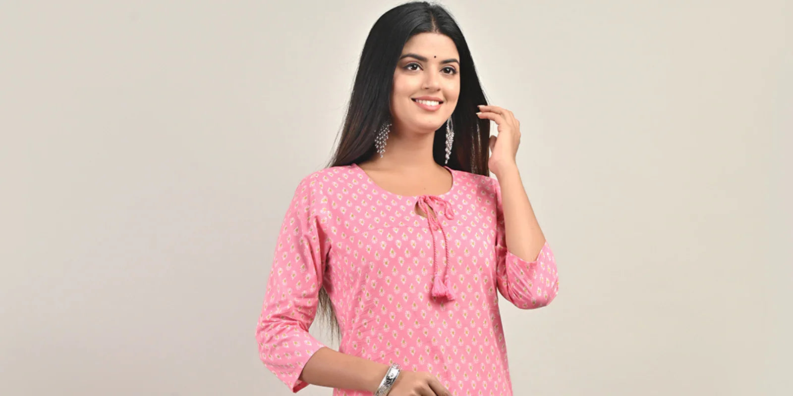 Smiling woman in pink straight kurti with 3/4 sleeves and silver earrings on beige background