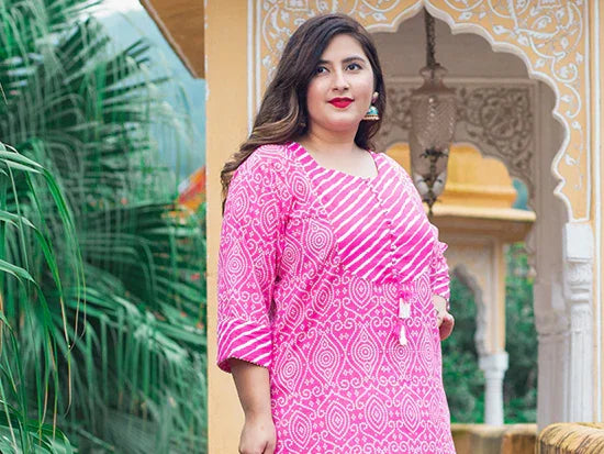 Woman in pink patterned kurta posing near traditional Indian architectural arch with greenery