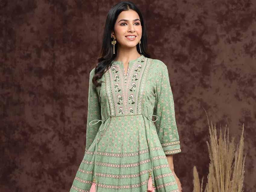 Smiling woman wearing a green embroidered ethnic dress with floral patterns against brown backdrop