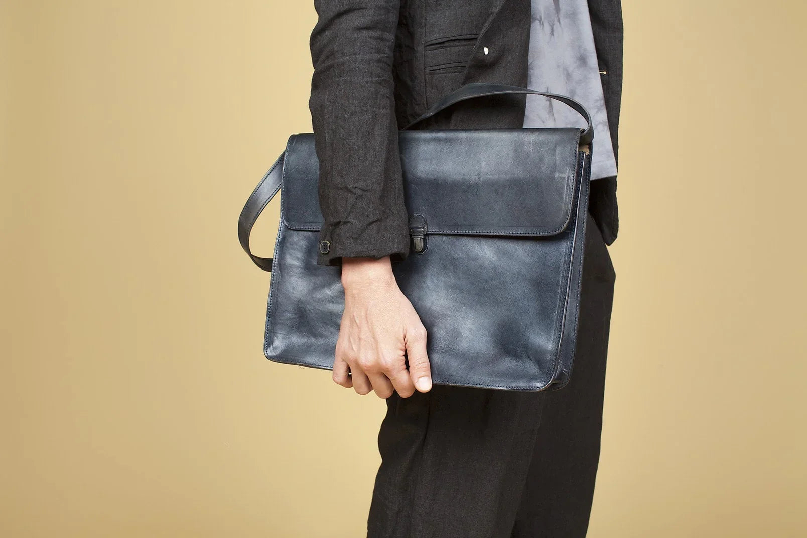 Person holding a black leather briefcase wearing a black suit against beige background