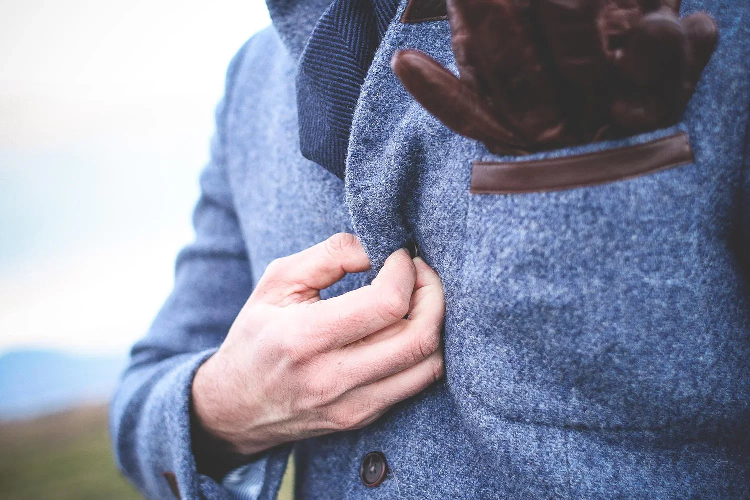 Close-up of a man buttoning a stylish blue wool jacket with brown leather gloves in pocket