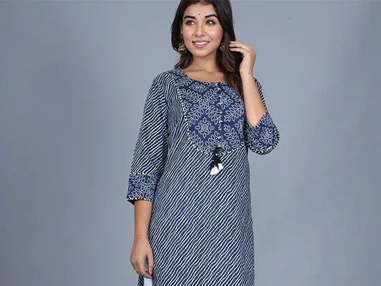 woman in blue and white patterned kurta with embroidered neckline and tassel detail, standing against grey background