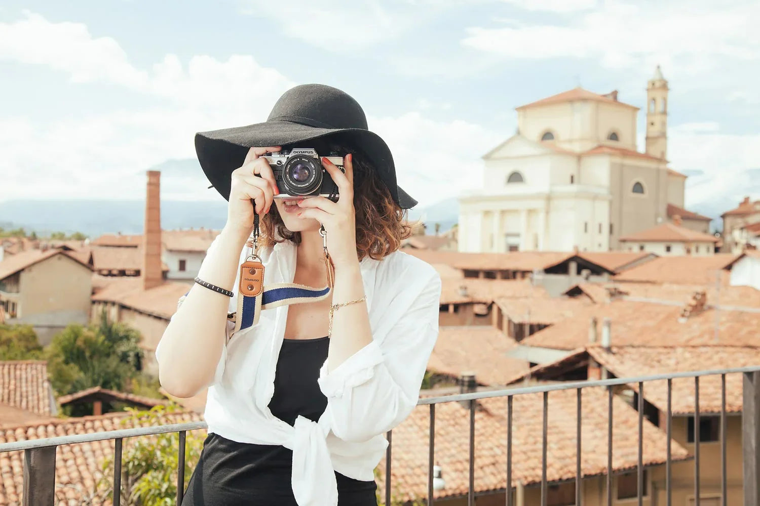 Young woman in black hat and white shirt taking photo with vintage camera in European town